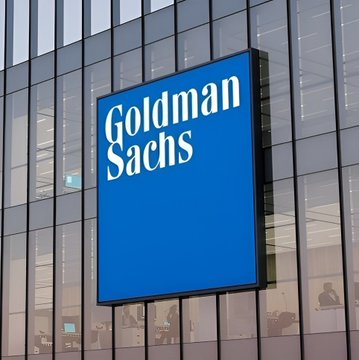 Goldman Sachs corporate logo sign in white text on a blue background, mounted on the exterior of a glass office building.