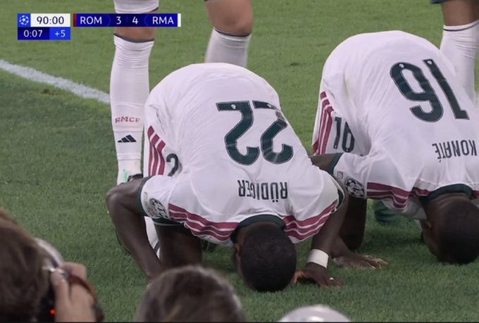 Real Madrid players Rüdiger (23) and Konaté (91) kneel on the pitch in prayer and celebration as the scoreboard shows ROM 3-4 RMA with 90:00 minutes played and +5 added time, capturing the dramatic moment of Real Madrid's incredible comeback from 1-3 down to lead 4-3 against Roma.