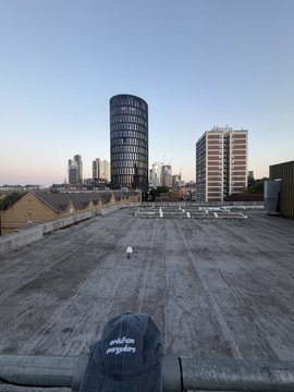 A rooftop view of a city skyline at dusk featuring a distinctive cylindrical tower building, with a black cap visible in the foreground.