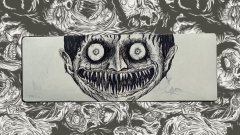 A creepy black and white illustration features a central rectangular panel displaying a wide, toothy grin face with staring eyes, framed by an ornate border of swirling decorative patterns.