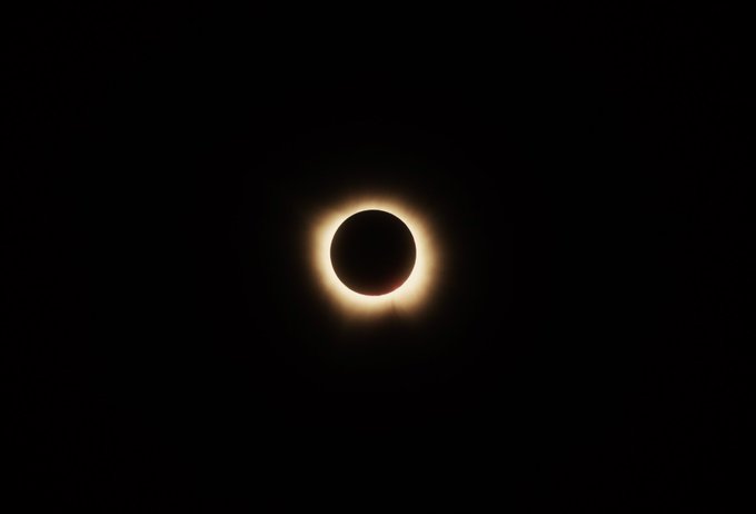 A total solar eclipse glows against a black sky, visually mirroring the post's metaphor of DOG traders "standing tall" through 13 consecutive rejections at the 50-day moving average, with the sun's corona encircling the darkened moon symbolizing the imminent "violent breakout" referenced in the caption.