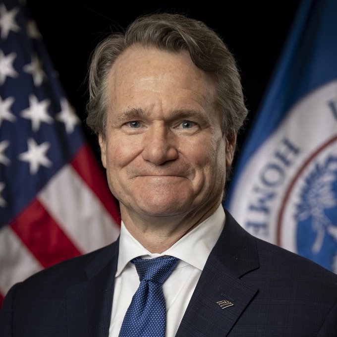 Bank of America CEO Brian Moynihan is pictured in a formal headshot, flanked by an American flag and what appears to be a Bank of America flag, visually representing the banking giant mentioned in the context of the $2.5 trillion institution exploring blockchain technology and its potential connections to Ripple and XRP.