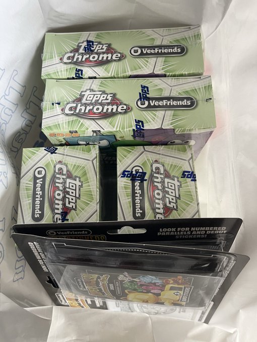 A white shopping bag containing several green boxes of 'Topps Chrome UEFA VeeFriends' trading cards and additional packaged merchandise.