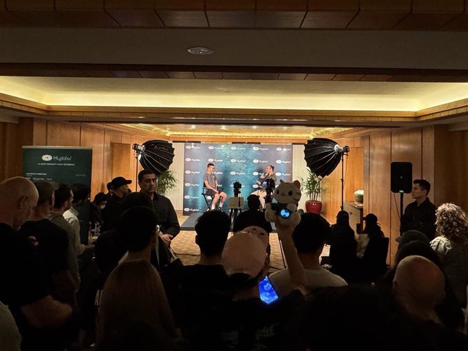 An audience gathered at what appears to be a 'Klabi' panel discussion or fan event, with photographers holding up a plush toy and phones toward a stage where speakers are seated.