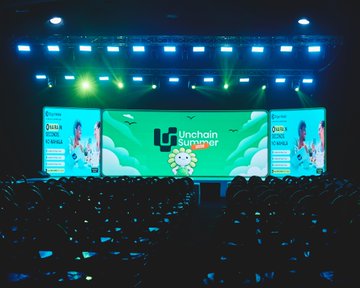 The image shows a large conference hall with a brightly lit stage featuring "Unchain Summer" branding on multiple screens, where an audience watches a speaker presenting about Web3 and blockchain innovations, including Bitget Wallet's Bank Transfer feature.