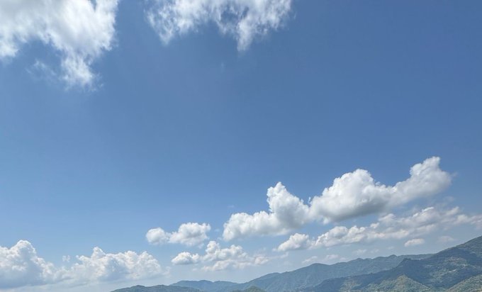 A serene blue sky dotted with scattered white clouds stretches above a distant mountain range, evoking a sense of openness and upward momentum—mirroring the optimistic, "risk-on" market sentiment described in the post, where three assets (BTC, a top L1, and a crypto-related stock like MSTR or COIN) are poised to rally together when liquidity flows freely.