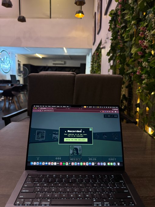A MacBook Pro sits open at a coffee shop with a colorful webpage titled "MEDICI 2615 EAST" displayed on the screen, along with a "Record" dialog box. The "made it in" caption suggests the laptop owner has arrived at the café shown in the background, which features hanging pendant lights and a lush plant wall.