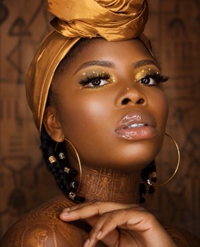 The image features a woman with dark hair wearing a gold turban, which is often associated with ancient Egyptian culture. She has her hand resting on her chin while looking directly at the camera. The background of the image includes a brown wall adorned with drawings that are related to the post about Nefertiti and Ancestra. The text in the image reads: "Nefertiti represents movement within Ancestra. Where Amina is stability, Nefertiti is discovery connecting RITUAL to major crypto assets and opening the path to broader markets. She is the bridge RITUAL vs the wider crypto world."