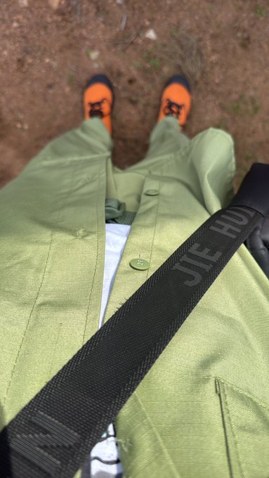 A first-person view shows someone wearing a light green jacket, black "JIE HUO" branded strap, and bright orange sneakers standing on a dirt path, with the "gm fam outside for tinubu" caption suggesting a morning outing in support of Tinubu.