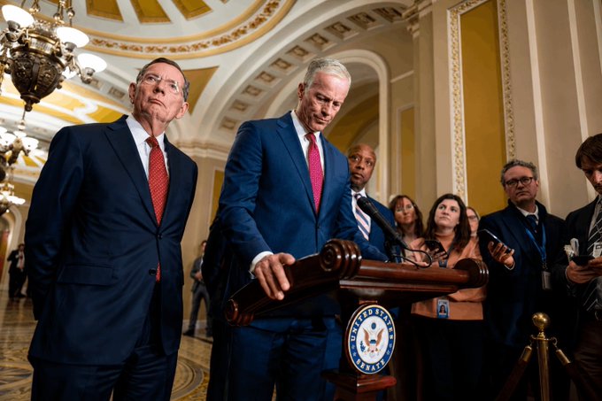 Two men in suits stand at a podium bearing the seal of the U.S. Senate, with one man speaking to reporters during a press conference in an ornate Capitol hallway. The scene aligns with the post's announcement about the Senate GOP releasing the final Clarity Act draft ahead of Tuesday's vote, suggesting a legislative update or statement on the bill.