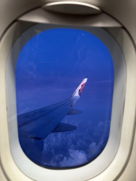 The image shows a view of an airplane wing through an airplane window. The perspective from inside the plane provides a unique vantage point, allowing passengers to see the sky outside with clouds below them. This scene captures the excitement and anticipation for the Algorand Developer Retreat after weeks of building, testing, debugging, and preparing. It's time to meet the community in person and participate in the semi-finals, ProcureAI challenge, and everything else that comes along with it.