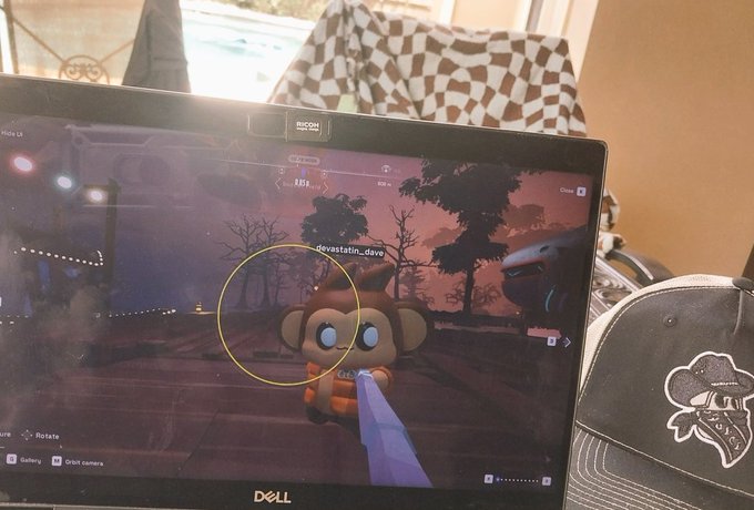 A Dell monitor displaying gameplay from a video game featuring a cute character in an orange outfit, with a baseball cap resting in front of the screen.