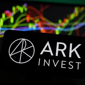 The **ARK Invest** logo is displayed on a smartphone screen in the foreground, with colorful stock market candlestick charts blurred in the background. This visual aligns with the announcement that Cathie Wood's ARK Invest has launched a tokenized venture fund on Ethereum for 24/7 trading, bridging traditional investment management with blockchain-based financial access.