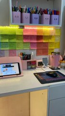 An organized desk setup featuring colorful wall-mounted pen organizers, sticky notes, a tablet, and various stationery items.