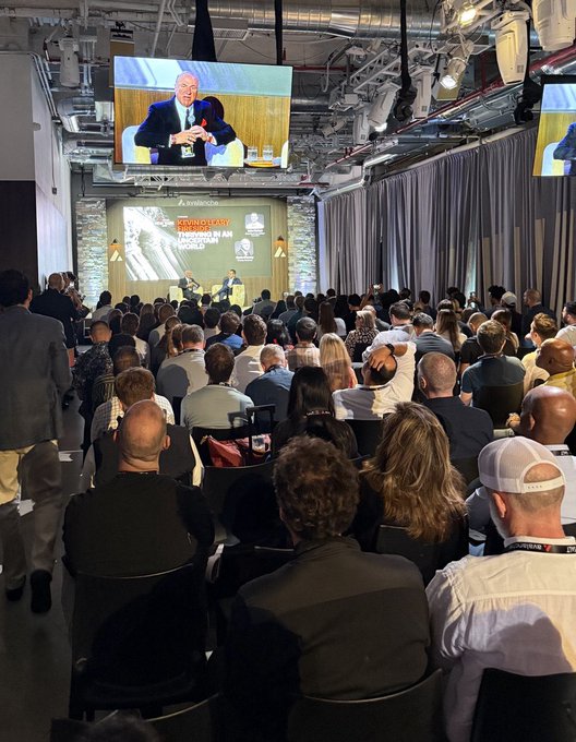 A packed panel room at the Avalanche Summit features a large screen displaying two speakers, with the "BARNBRIDGE" sponsor logo visible, contradicting the sentiment that "nobody likes Avalanche" given the substantial audience turnout. Visible signage includes "RWA ROADS" indicating a discussion on real-world assets.