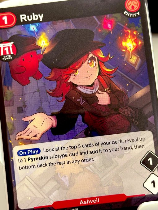 A 'Ruby' trading card (cost 1, Entity type) by Ashveil, depicting a red-haired character in a black hat with the ability: 'On Play - Look at the top 5 cards of your deck, reveal up to 1 Pyreskin subtype card and add it to your hand, then bottom deck the rest in any order.'