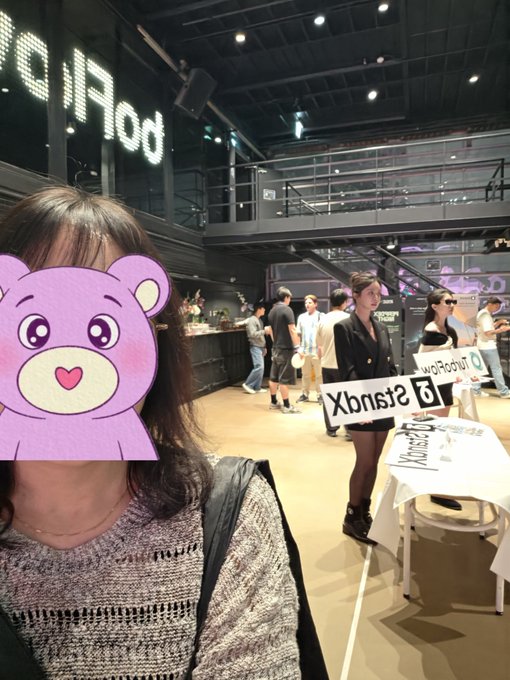 A casual selfie inside a Polkadot-themed venue with industrial decor, where a person's face is obscured by a purple bear cartoon sticker.