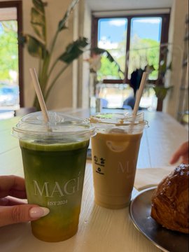 Two iced drinks are shown at a café called 'MAGI EST 2020', one green (likely matcha) and one brown (likely iced coffee), alongside a pastry on a plate.