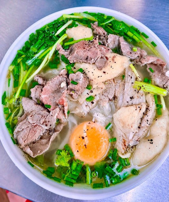 A bowl of Vietnamese pho with beef slices, an egg yolk, green onions, and noodles in a clear broth.