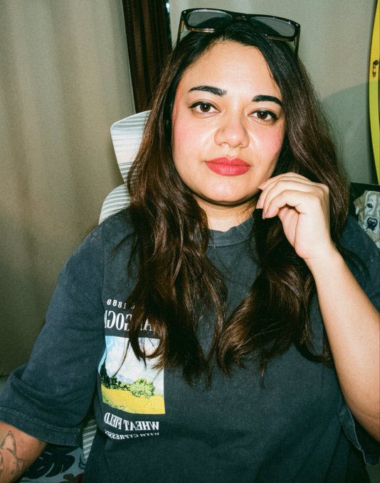 Portrait photo of a woman with long dark hair and red lipstick, wearing a gray t-shirt with sunglasses on her head.