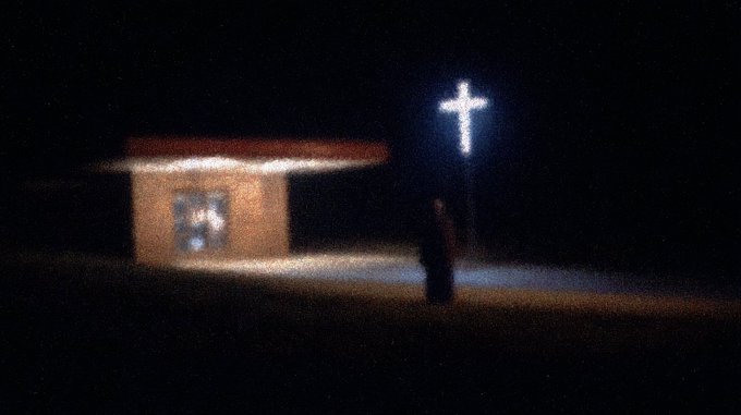 A glowing illuminated cross stands in a dark, shadowy landscape next to a small building, where a solitary figure approaches toward the light. The image evokes themes of spiritual searching and redemption, aligning with the NFT auction title "Seeking Healing" featured on the ninfa.io platform.