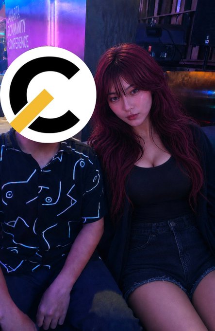 The image shows a woman with long red hair in a black top and denim shorts sitting next to a person whose face is covered by a logo, at an event with purple lighting in the background. A banner in the background reads "CREATING COMMUNITY CONFERENCE," and the post reflects on her nervousness about getting to take a photo with the "big sis" at the event hosted by @xiordaily.