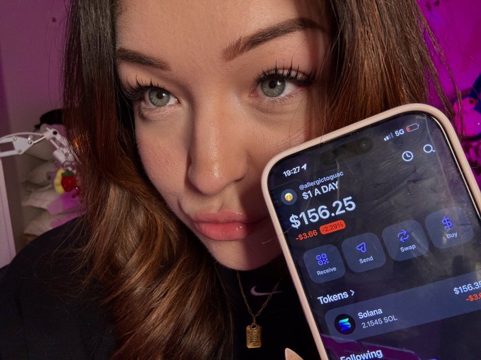 The image features a woman holding up her cell phone, which displays a message about buying Bitcoin at $1 per day for 210 days. The text on the screen reads "day 210 of buying $1 worth of sol until ath". This suggests that the woman is considering investing in Bitcoin and has chosen to invest over a period of 210 days, purchasing Bitcoins at $1 each day.