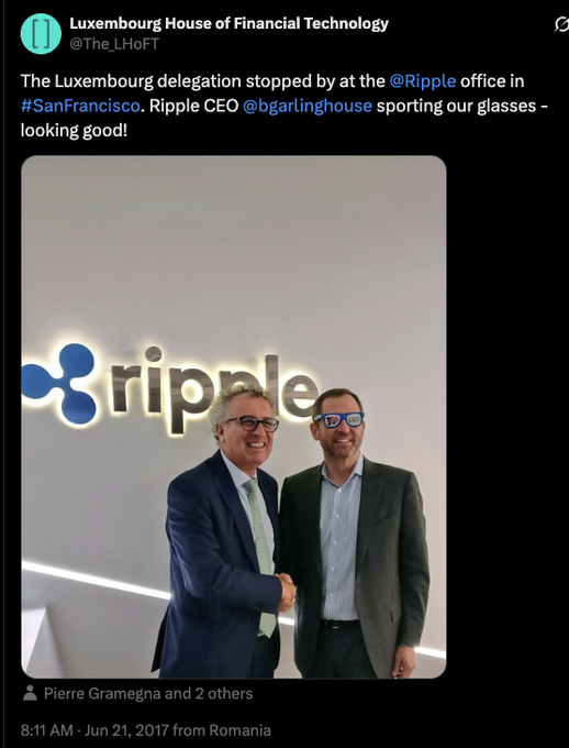 The image shows two men standing in front of a white wall with a Ripple logo displayed above them, both wearing suits and glasses. One man has his hand placed on the other's shoulder as they pose for the photo. The background features a clock that reads "8:11", indicating it is 8:11 am. The post includes text about Ripple, which suggests that the men are involved in or have knowledge of Ripple coins.