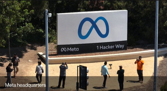 The image shows a group of people standing around a large white sign with an "M" logo at the center. The sign displays the words "Meta just started paying creators in USDC stablecoins." This indicates that Meta, the social media platform, is now accepting payments from its users in the form of USDC stablecoins. The image also includes a caption about the real issue surrounding this payment method and how it relates to the post.