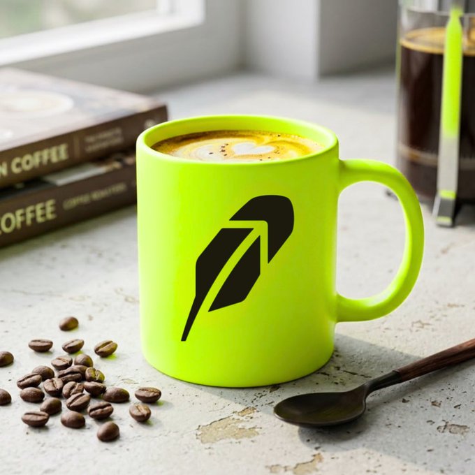 A bright green mug with the Robinhood logo sits beside coffee beans, a spoon, and coffee containers. The post’s “Hood morning” greeting and message to “make Robinhood bigger today” tie into the branded morning coffee scene.