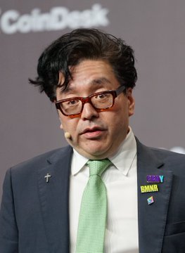 A man in a suit and green tie speaking at a CoinDesk event, wearing glasses and a 'BNNK 2024' badge.