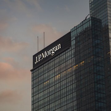 A JPMorgan office tower bears the prominent “J.P. Morgan” sign against a dusk sky. The image accompanies news that the bank has made its tokenized money market funds MONY and JLTXX available on Solana to qualified U.S. investors through Morgan Money.