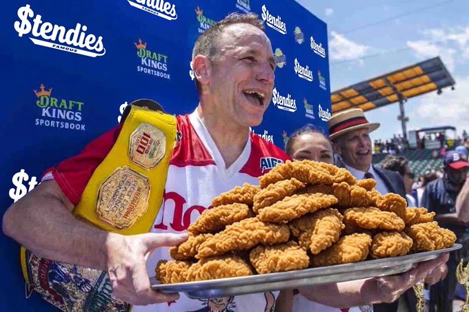 A man wearing a Phillies baseball jersey and a yellow championship belt excitedly holds a large silver platter piled high with fried chicken tenders.