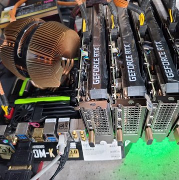 The image shows an open-air mining rig with three NVIDIA GeForce RTX graphics cards installed, alongside a large CPU cooler on the motherboard, illustrating the evolution from early Bitcoin CPU mining to modern GPU-based cryptocurrency mining operations.