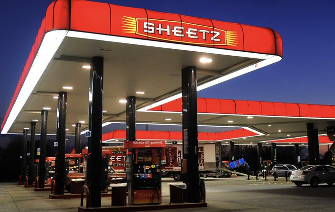 A brightly lit 'SHEETZ' gas station canopy at dusk, featuring its signature red signage and illuminated pumps with several cars parked nearby.