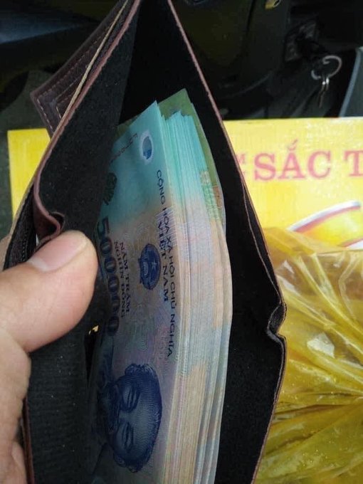 The image shows a hand holding an open wallet with several stacks of Vietnamese money inside. The wallet appears to be filled with cash, indicating that the person might have received or is planning to spend a significant amount of money. The photo also includes text in the caption, which seems unrelated to the main focus on the wallet and its contents.