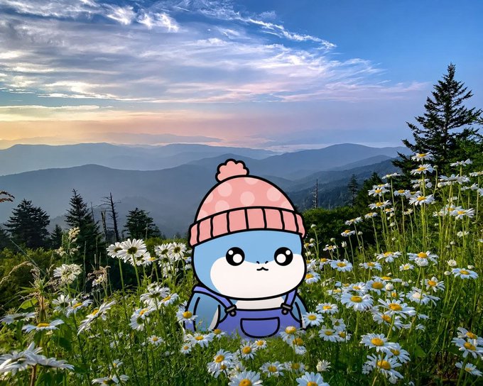 A cartoon blue seal-like character wearing a pink polka-dot beanie and purple overalls, superimposed over a scenic mountain landscape with daisies in a field at sunset.