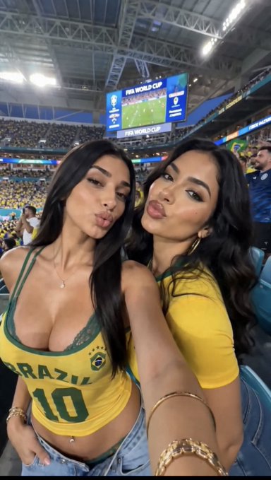 Two female fans wearing Brazilian jerseys—one displaying "BRAZIL 10"—take a selfie at a FIFA World Cup stadium, with the scoreboard and "FIFA WORLD CUP" signage visible in the background, perfectly matching the post's prediction matchup between Brazil and Japan.