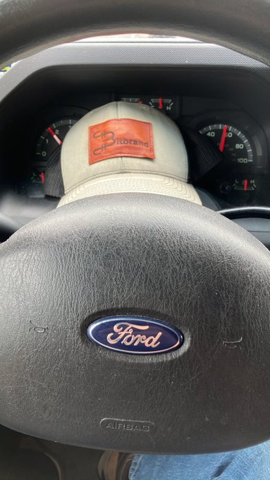 An interior shot of a Ford vehicle showing the steering wheel with the blue Ford logo and a tan Carhartt cap resting on the dashboard in front of the speedometer.