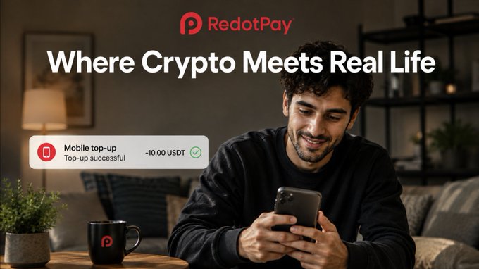 A RedotPay advertisement featuring a man smiling at his phone, with the tagline 'Where Crypto Meets Real Life' and a notification showing a successful 'Mobile top-up' for -10.00 USDT.