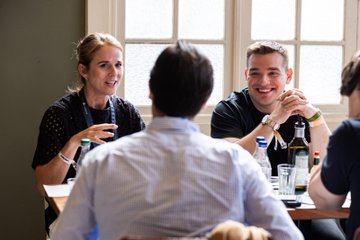 Two groups of professionals engage in a lively conversation around a table, with smiling faces suggesting a productive networking session. The image reflects the post's theme of ecosystem partnership and builder collaboration, visually reinforcing the meeting between River Inc. and BNB Chain founders.