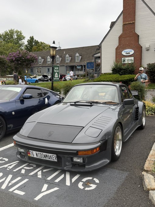 A gray Porsche 911 with a "T6 WIDOWMAKER" license plate is parked in a lot outside what appears to be "Village Centre Pools," with a few people milling about in the background — a fitting scene for the prompt's "touch some grass" sentiment, as the car meet offers a chance to step outside and enjoy the day.