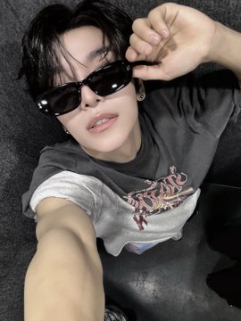 A young man wearing black sunglasses and a graphic t-shirt poses for a close-up selfie, adjusting his hair with one hand. The casual, stylish photo complements the post's hashtags promoting the artist/brand "ALPHADRIVEONE" (ALD1) and "XINLONG."