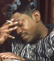 A man with dark curly hair wearing a patterned shirt holds his hand to his forehead in a facepalm gesture.