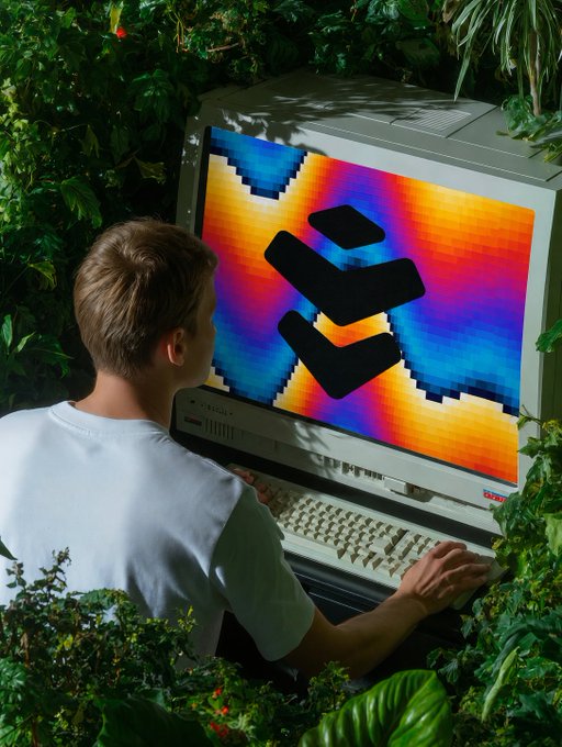 A young person in a white shirt sits at an old CRT computer displaying a colorful Bitcoin logo screen, surrounded by lush green foliage.