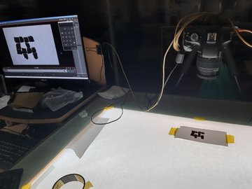 A photography setup featuring a monitor displaying an image, a camera, and a small target marker on a white surface.