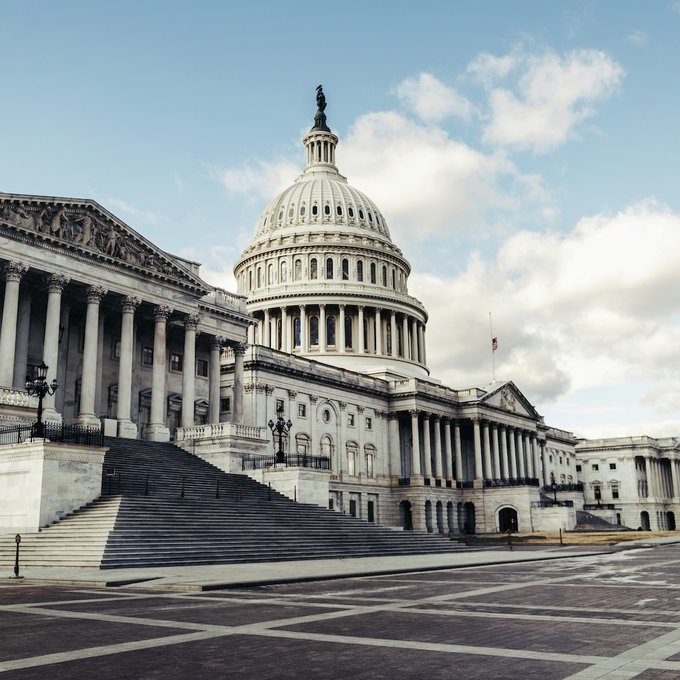 The United States Capitol building stands under a partly cloudy sky, its iconic dome and grand staircase visible from the street below. The image relates to the post by visually representing the legislative venue in Washington, D.C., where debates over the CLARITY Act and stablecoin regulation are taking place.