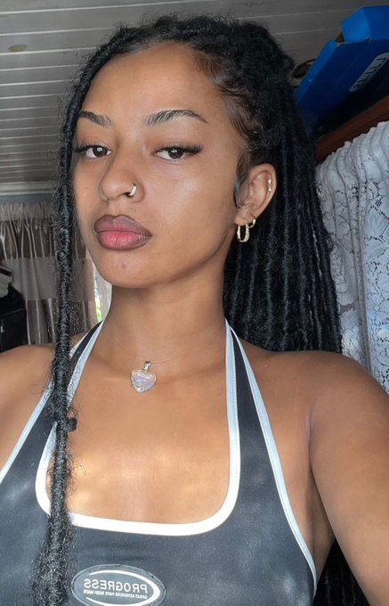 A selfie of a young woman with long locs, a nose ring, and hoop earrings, wearing a black and white halter top with a heart pendant necklace.
