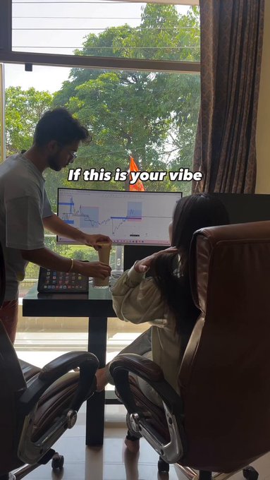 Candid photo of a man standing and pointing at a trading chart on a monitor while a woman sits in an office chair, overlaid with the text 'If this is your vibe'.
