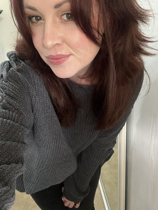 A selfie of a young woman with reddish-brown hair wearing a gray knit sweater.